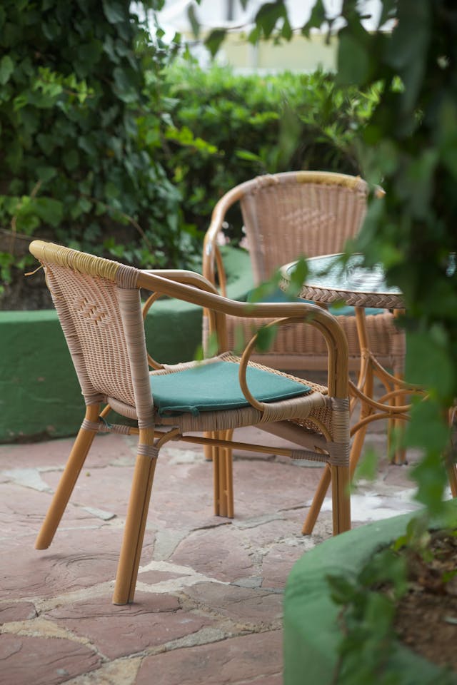 Outdoor wicker chairs and matching table in a tranquil garden setting with lush greenery. Image via Pexels