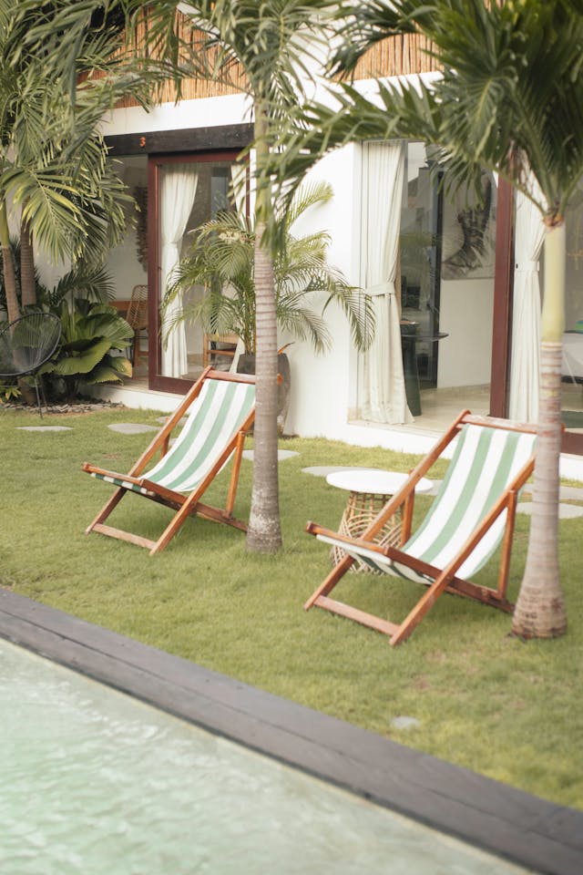 Wooden lounge chairs near palm trees and pool. Image by Pexels