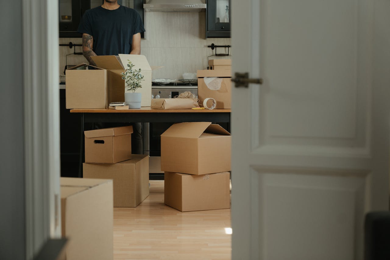 Person in a black shirt standing near brown cardboard boxes. Image by Pexels