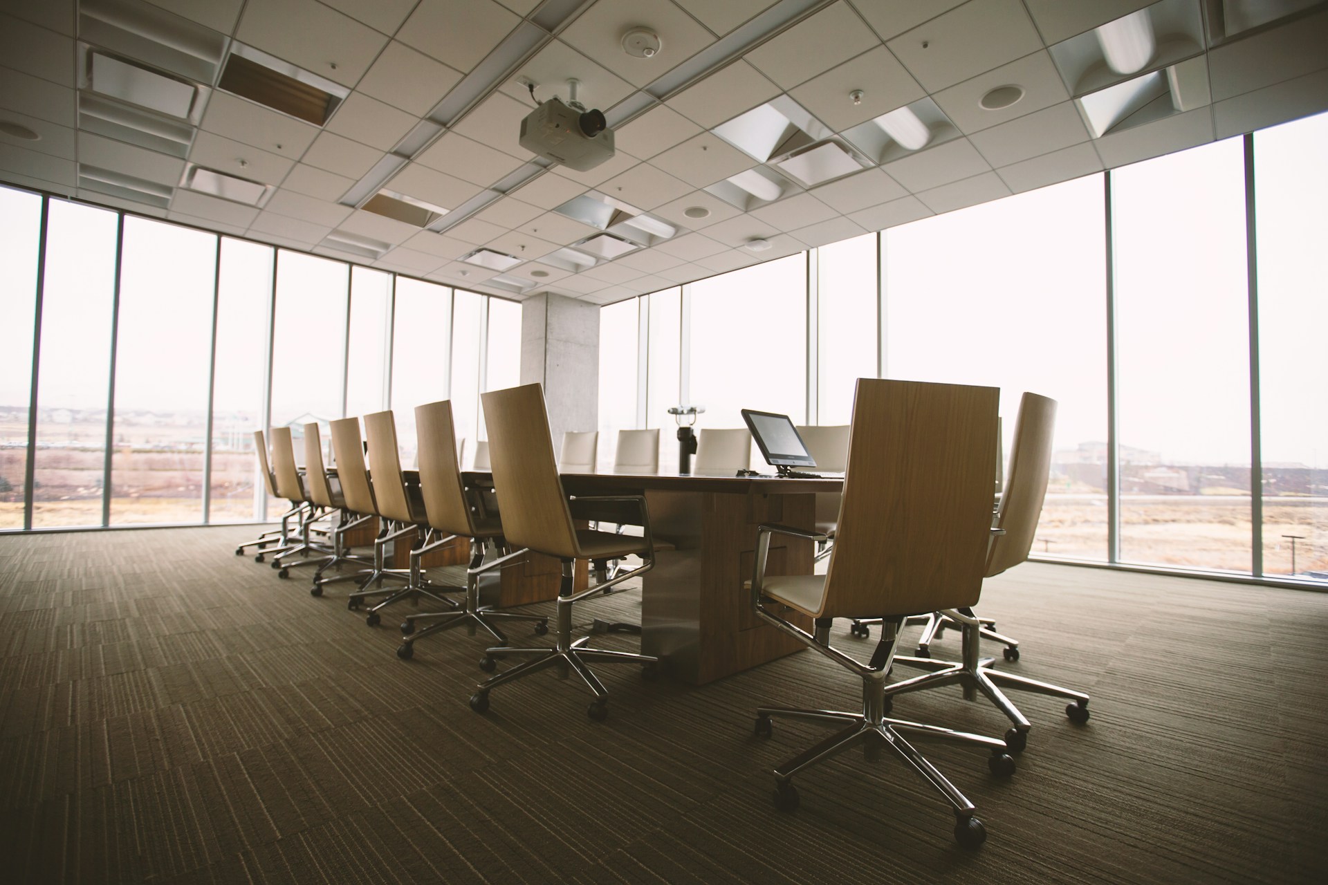 Oval brown wooden conference table and chairs in a conference room. Lots of floor to ceiling windows. Image by Unsplash