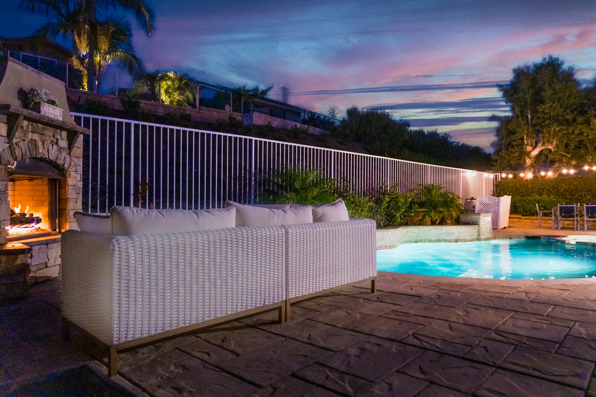 Patio with furniture, outdoor fireplace and a pool at night. Image by Unsplash