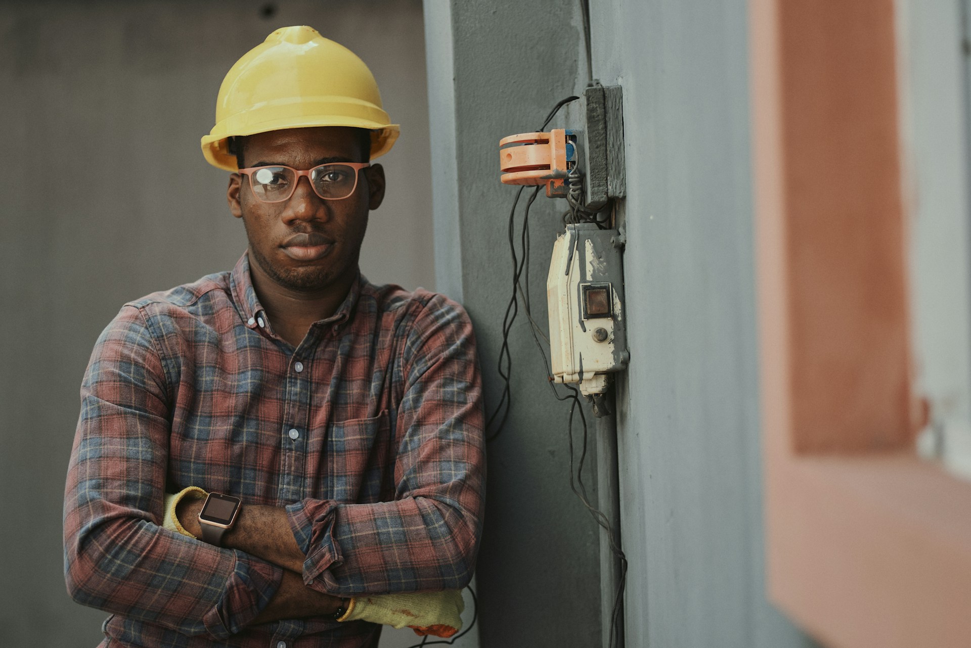 Contractor in plaid shirt and yellow hard hat holding tools at a job site. Image via Unsplash