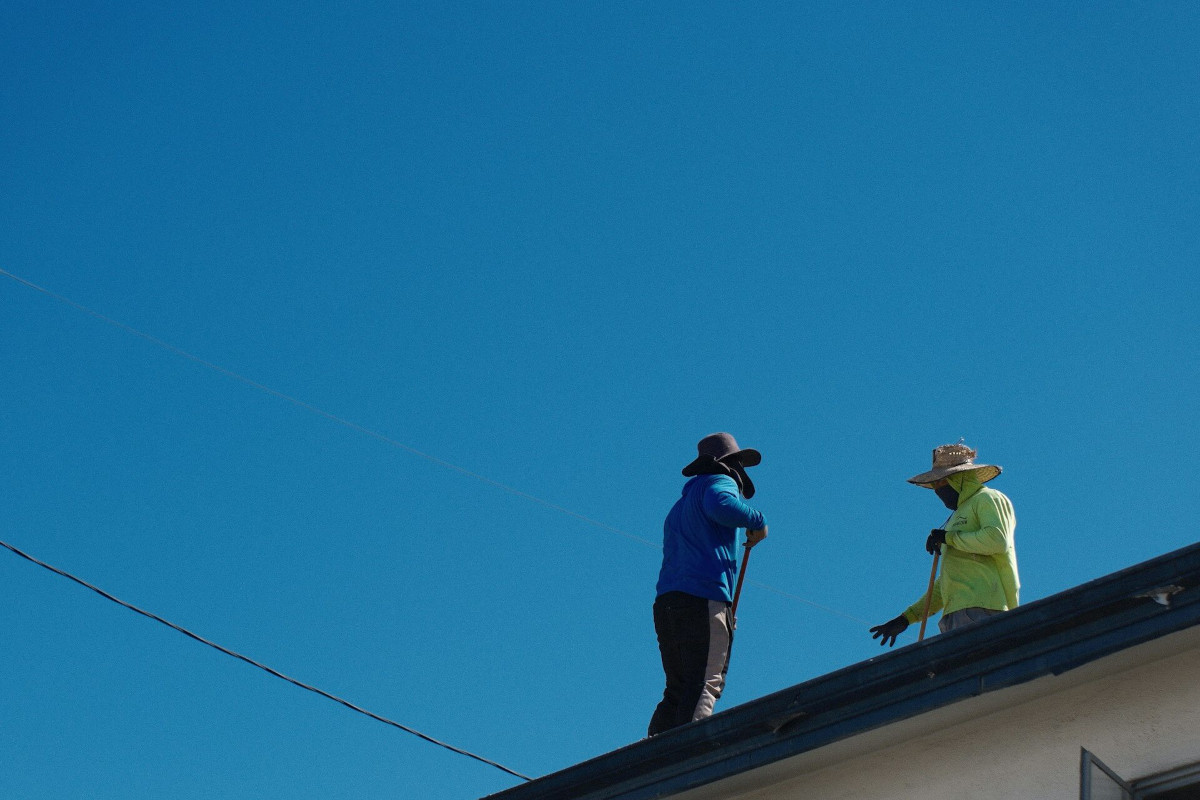 A roofing contractor inspecting shingles on a residential roof. Photo by Hershy Kulkarni on Unsplash
