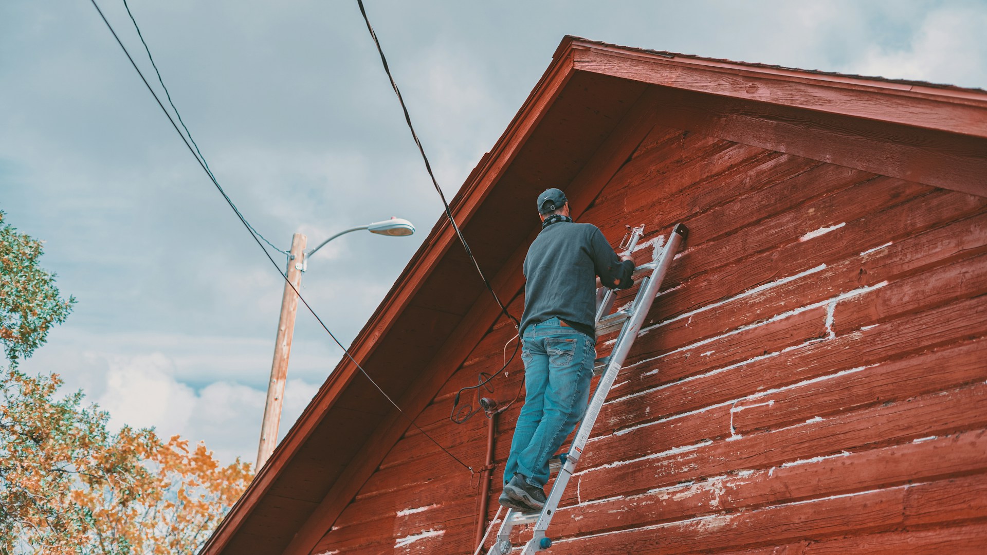 A person on a ladder painting the side of a building red. Image by Unsplash