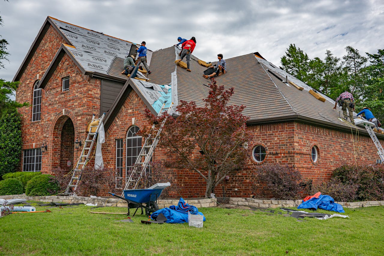 Roofing workers renovating shingles on a brick rental house. Image via Pexel
