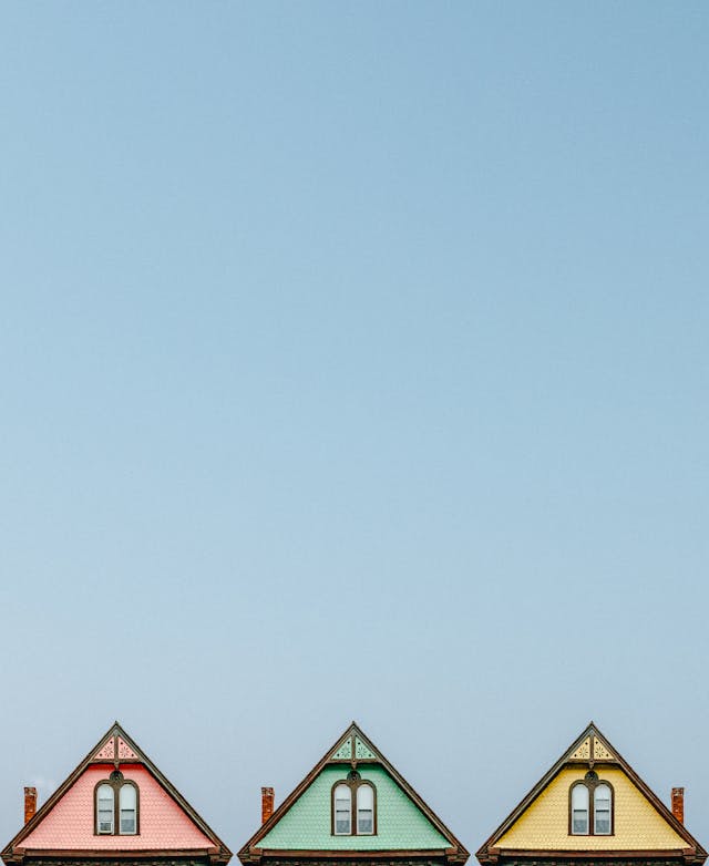 Three houses, one pink, one green, one yellow. Large blue sky. Image by Pexels