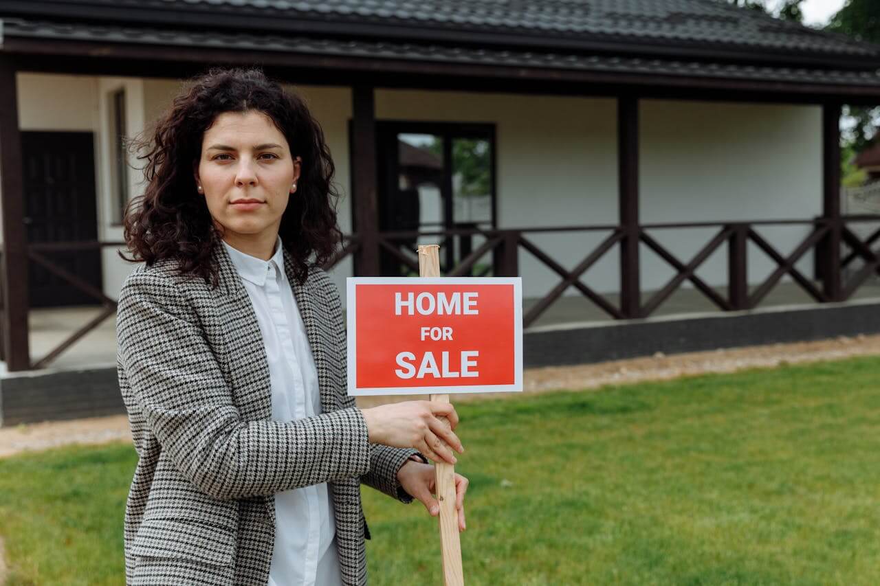 Real estate agent holding a home for sale sign. Image by Pexels