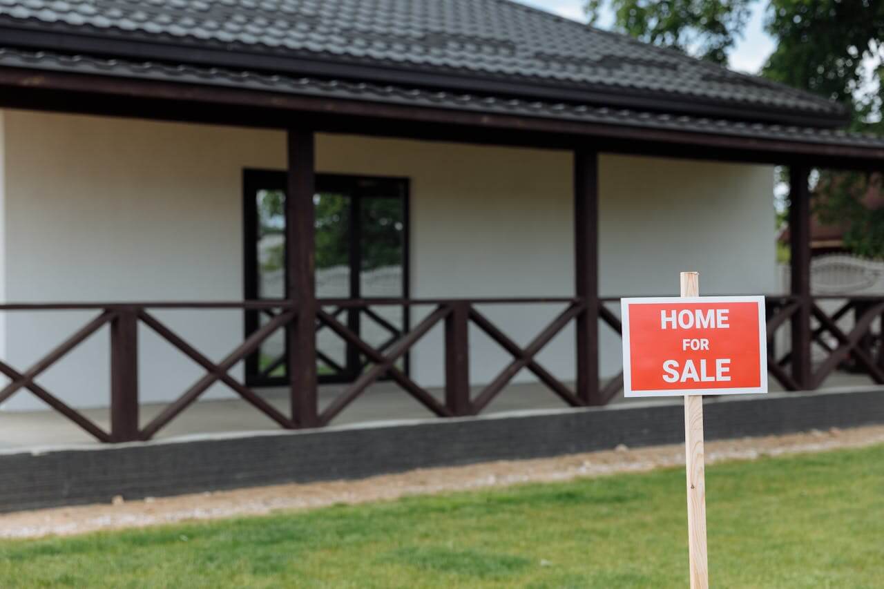 house with red and white for sale sign on the lawn. Image by Pexels