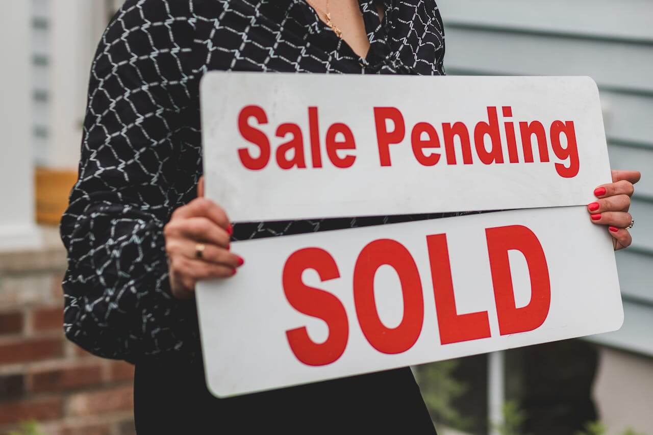 Person holding a for sale/sale pening sign. Image by Pexels