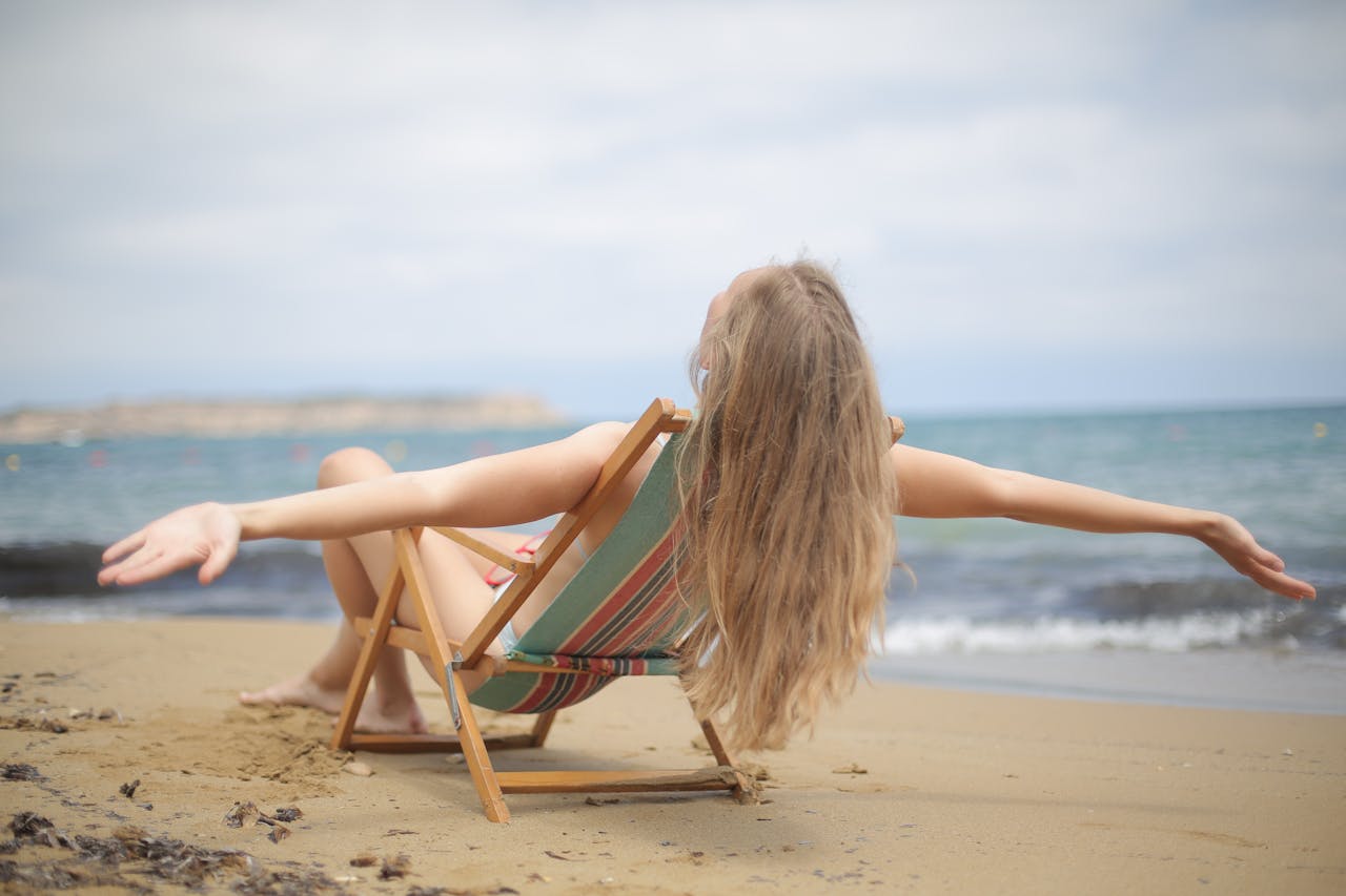 Woman sitting on folding chair on a beach. Image by Pexels