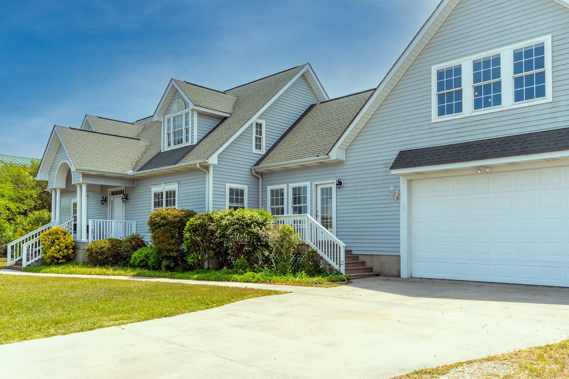A grey house with a large driveway in front of it representing a rental property being sold. Image by Unsplash