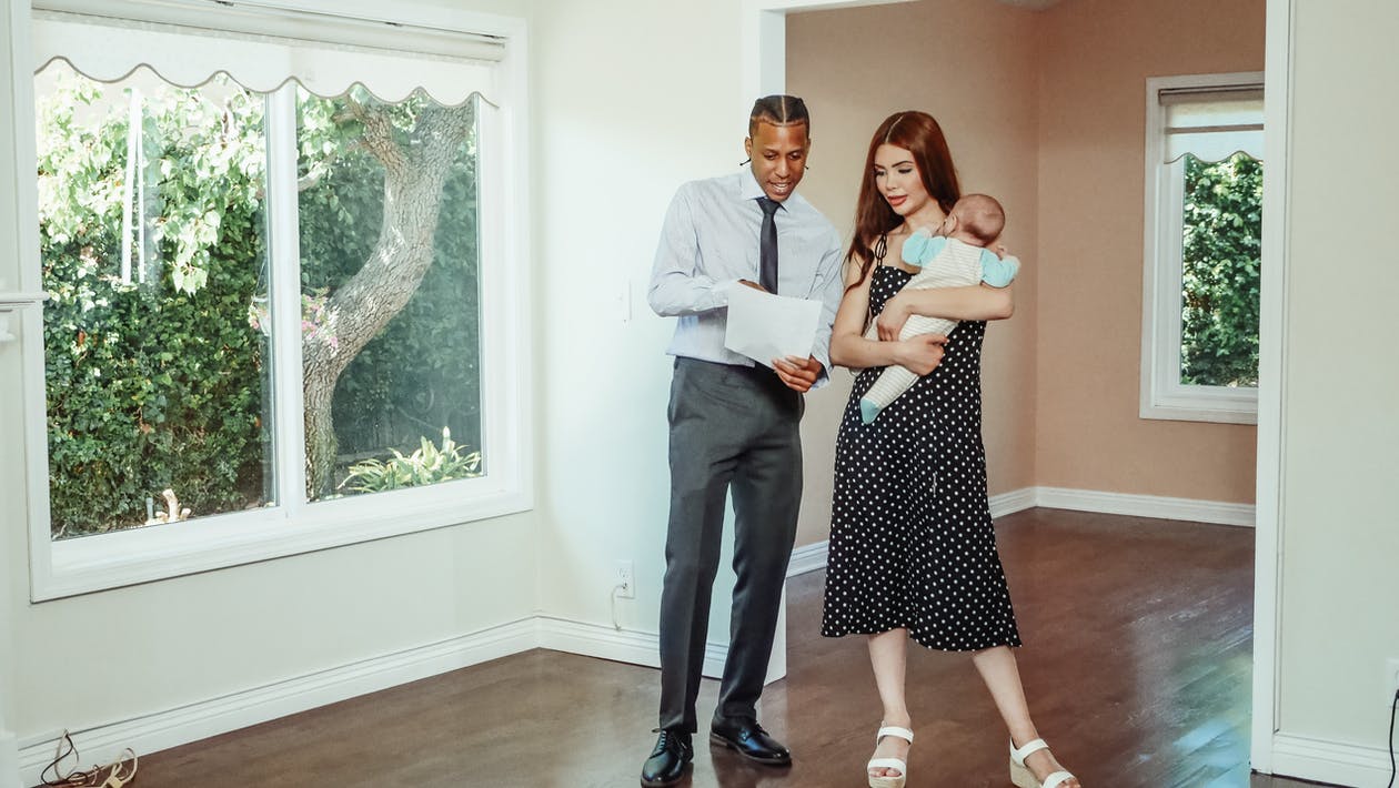 A man holding paper talking to a girl holding a baby in a house