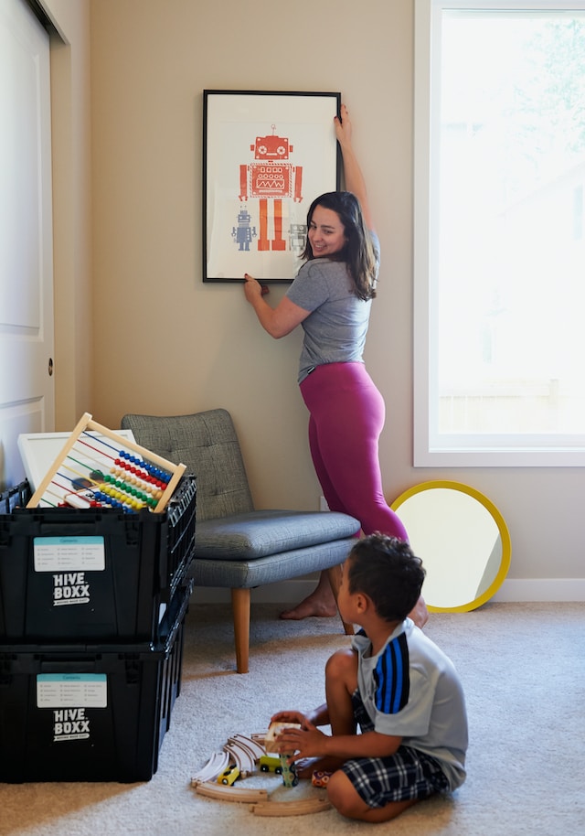 person haning a picture on a wall, child playing on the floor