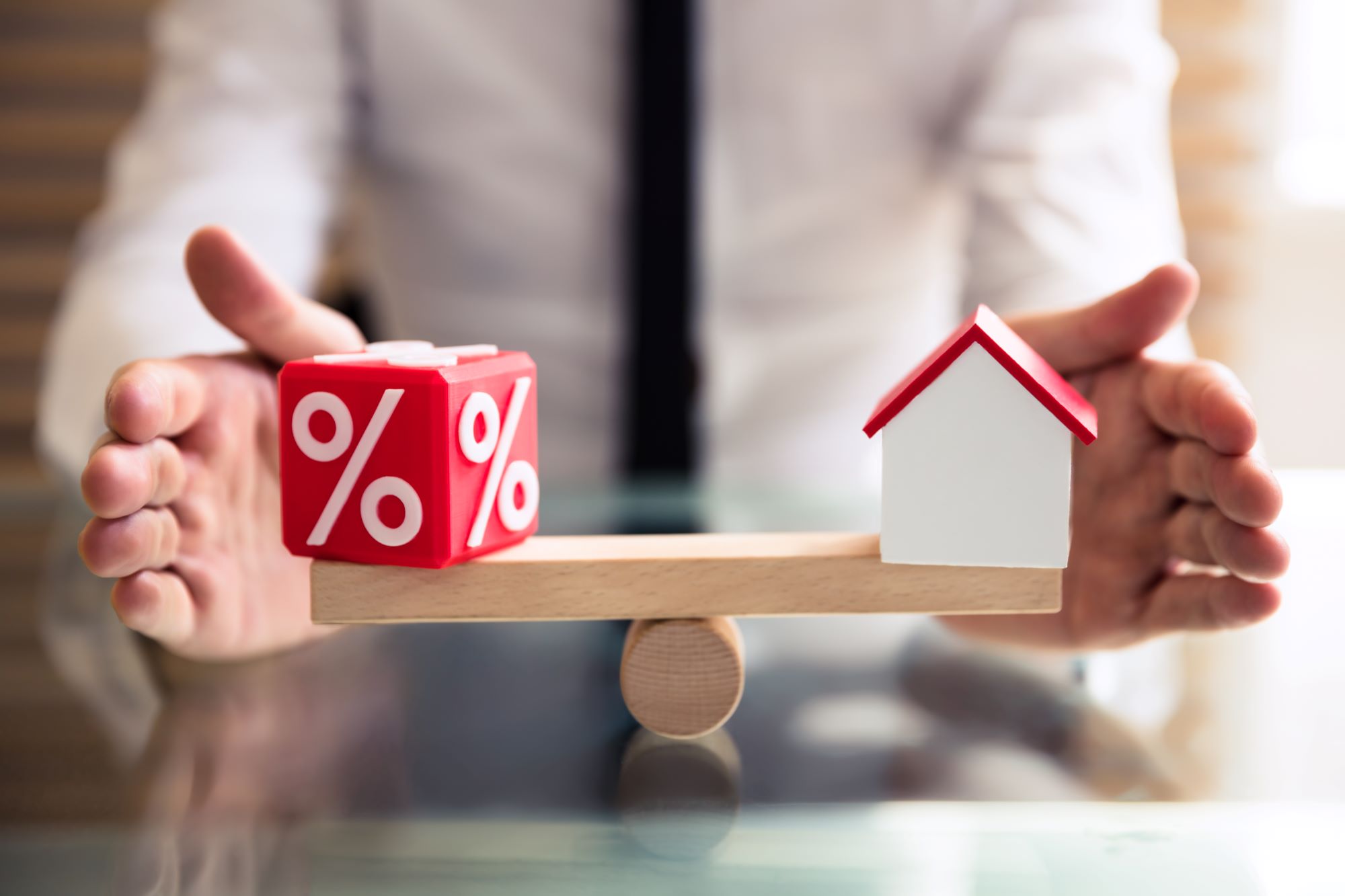 a red dice with % on it and a house on a seasaw made out of wooden blocks. Person in background with a black tie