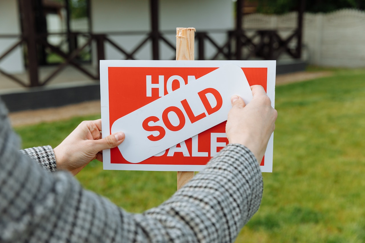 person putting a sold sticker on a for sale sign