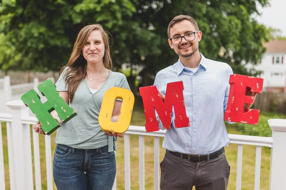 2 people holding up the letters H O M E (home)