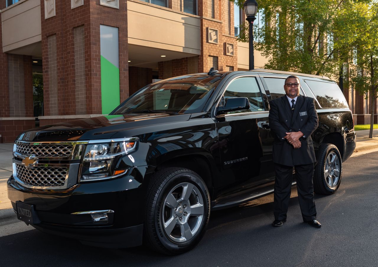 Chauffeur standing by luxury black SUV outdoor. Image by Pexels