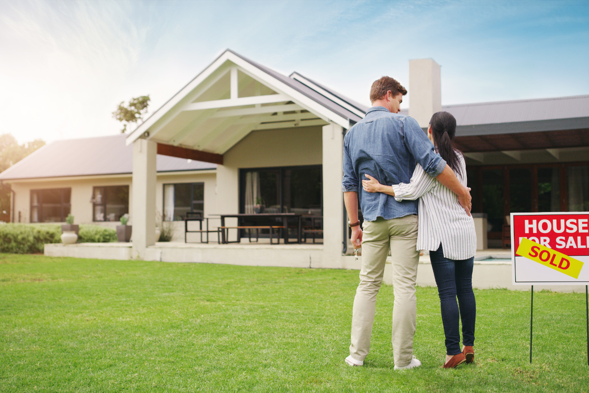 a couple standing in front of a house that has a sold sign on the lawn