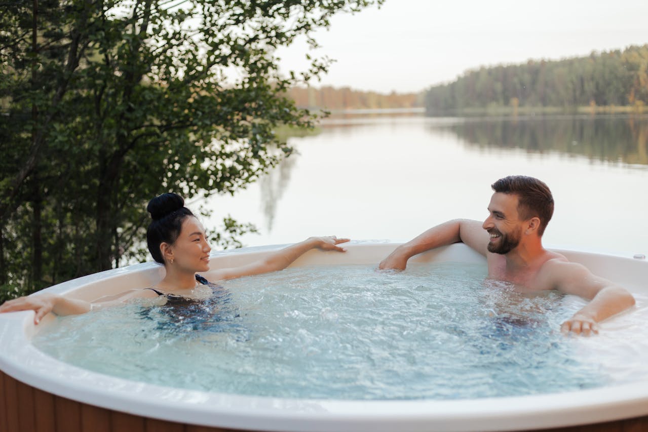 2 people in a hot tub, lake in the background. Image by Pexels