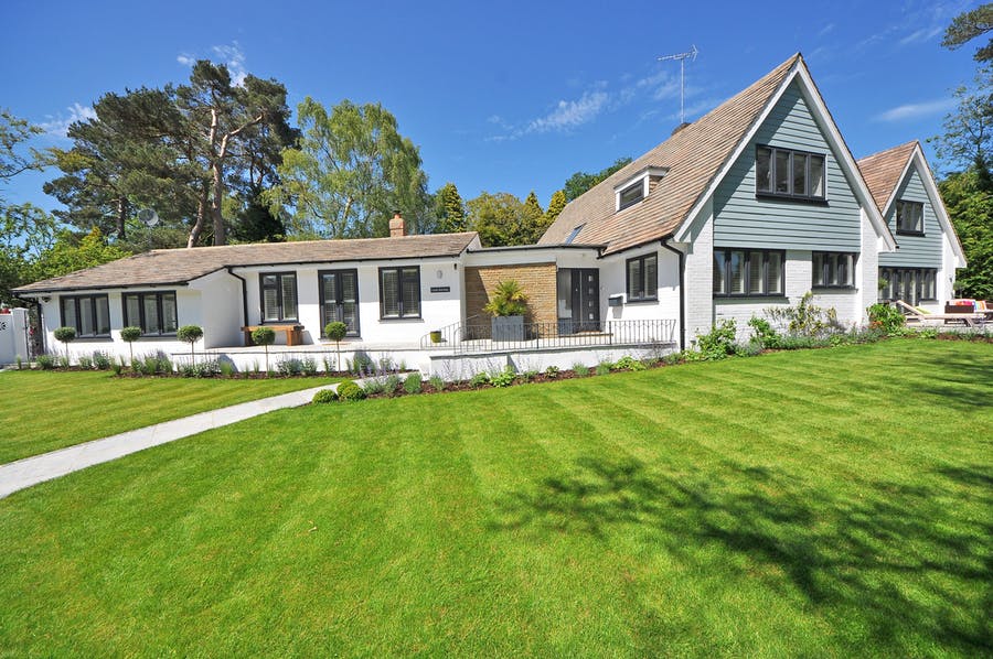 Large white and grey house, trees behind the house, large gras area in front of the house