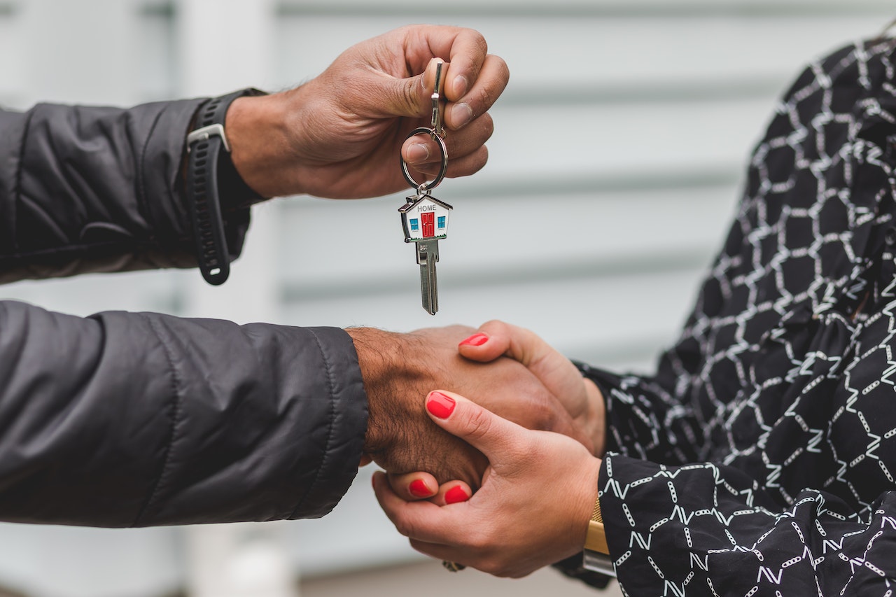 person handing over a silver key that looks like a house on top