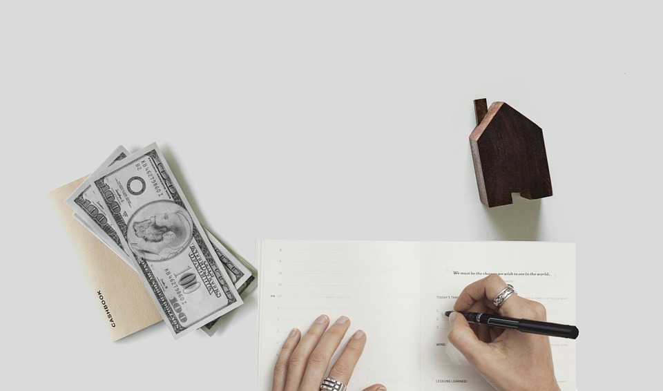 money and house on a table, person writing a note